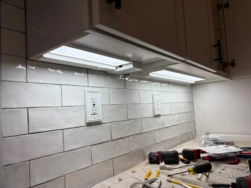 Under-cabinet LED light bars installed above a tile backsplash with GFCI outlets